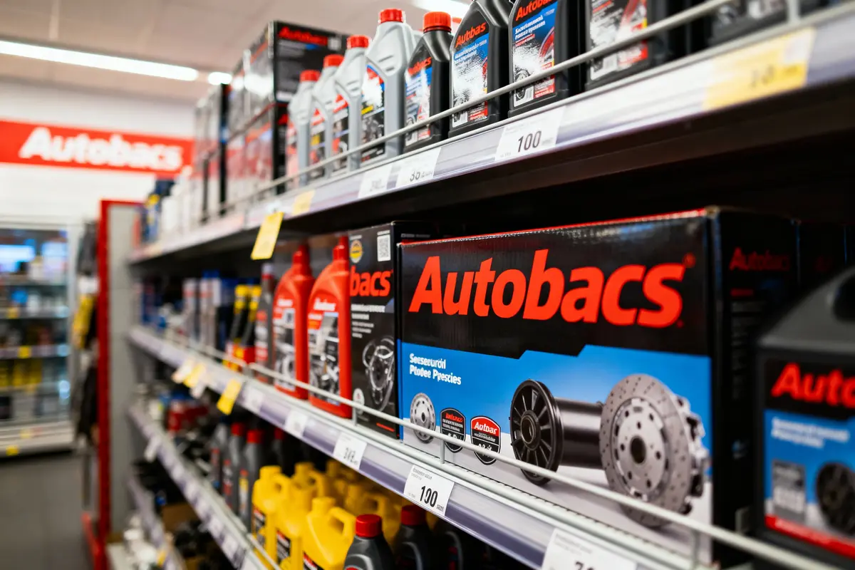 Rayon de magasin avec produits Autobacs, huiles et pièces automobiles, prix affichés sur étagères.
