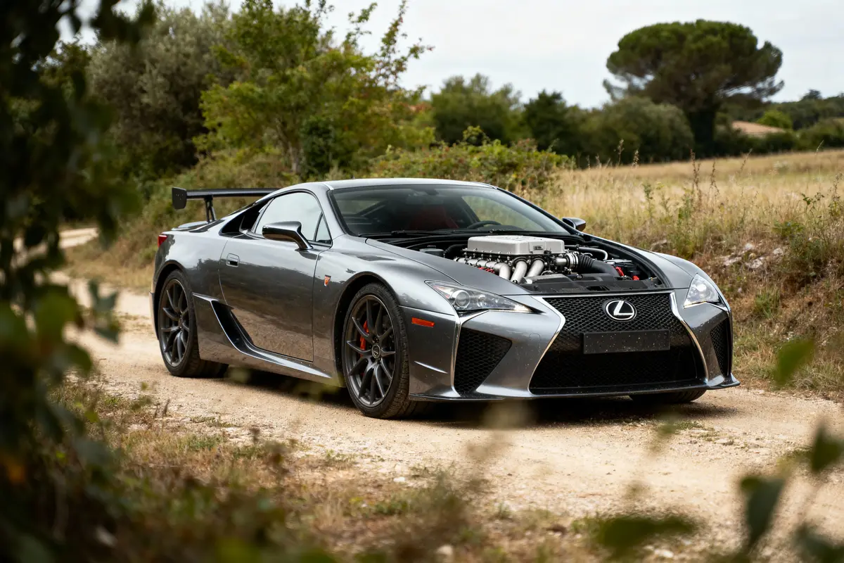Voiture de sport Lexus grise, garée sur un chemin terreux, avec le capot ouvert, montrant un moteur haut de gamme.