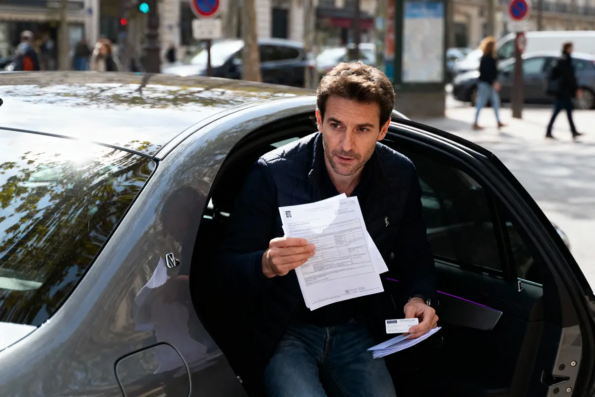 Un homme sort d'une voiture tenant des documents officiels dans une rue animée.