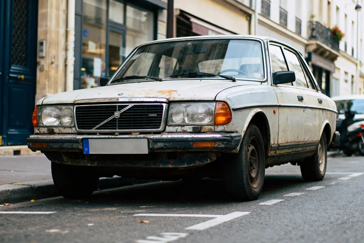 Voiture ancienne Volvo, peinture écaillée et rouillée, garée sur un trottoir dans une rue urbaine.