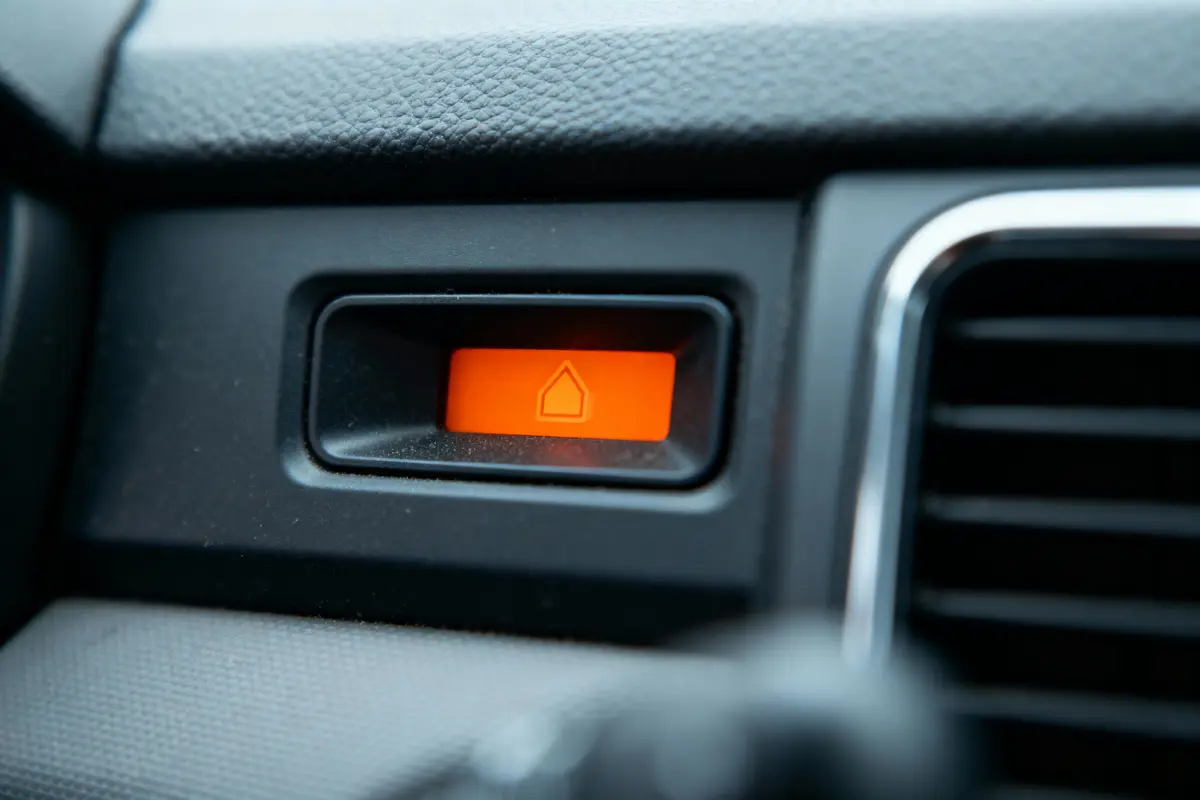 Bouton orange de forme de maison sur le tableau de bord d'une voiture, entouré de matériaux en plastique texturé.