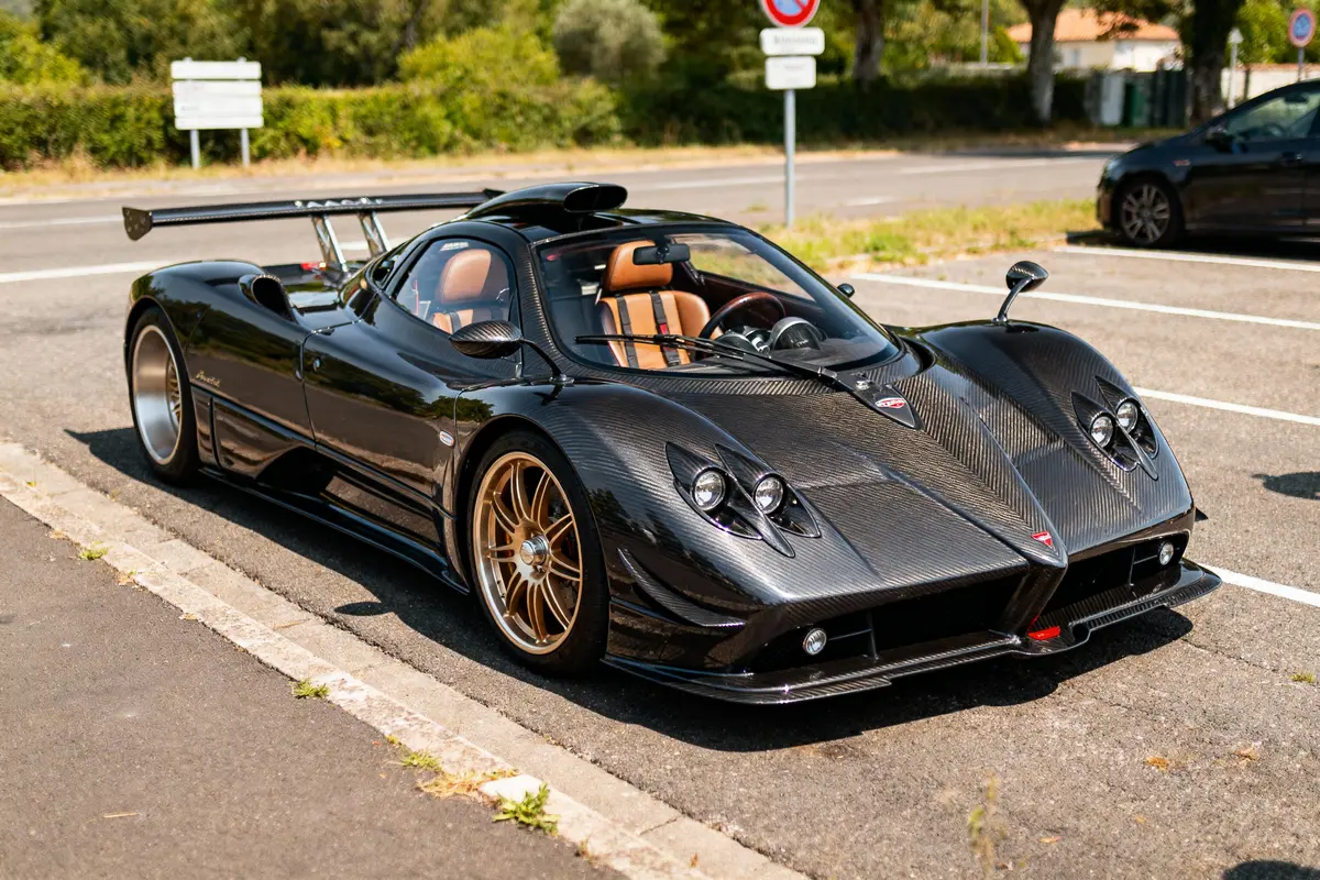 Voiture de sport noire stationnée, design aérodynamique et intérieur cuir, soleil éclatant.
