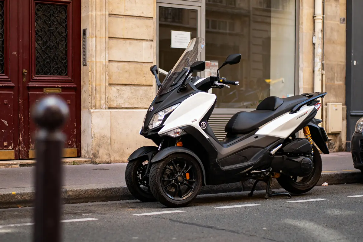 Scooter blanc et noir garé sur un trottoir urbain, devant un bâtiment en pierre beige.