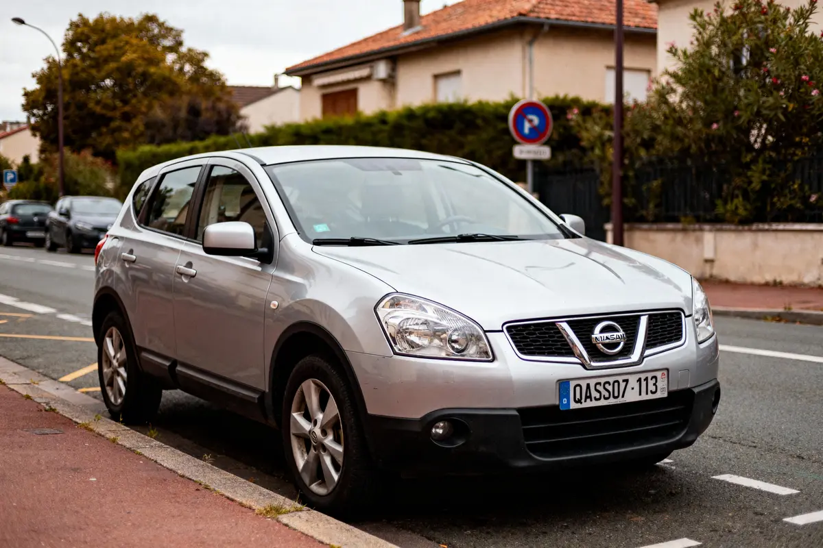 SUV gris Nissan stationné sur une rue résidentielle avec maisons et panneau d'interdiction en arrière-plan.
