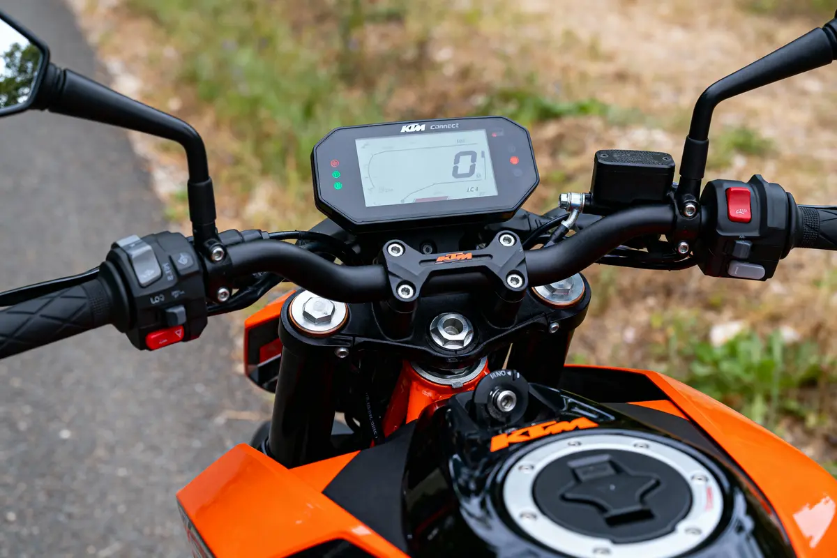 Guidon de moto KTM avec tableau de bord numérique, commandes et réservoir visible en arrière-plan.