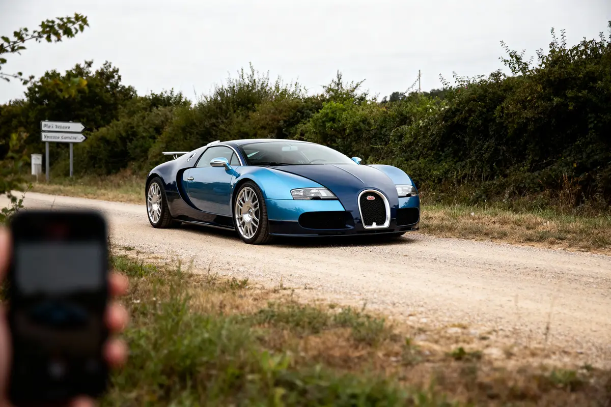Voiture de sport bleue sur un chemin de terre, entourée de verdure, photographiée de côté.