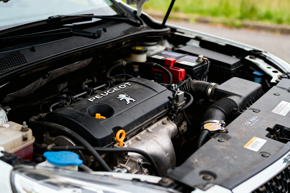 Moteur de voiture Peugeot avec capot ouvert, montrant composants et câblage à l'intérieur du compartiment moteur.