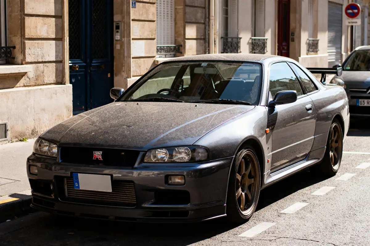 Voiture sportive grise garée dans une rue, légèrement poussiéreuse, avec jantes en alliage bronze.