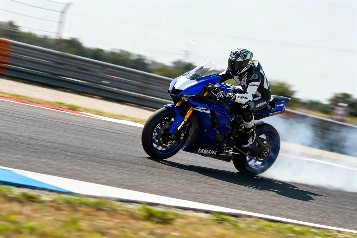 Motard en combinaison noire et blanche, pilote une moto Yamaha bleue sur circuit, générant de la fumée.