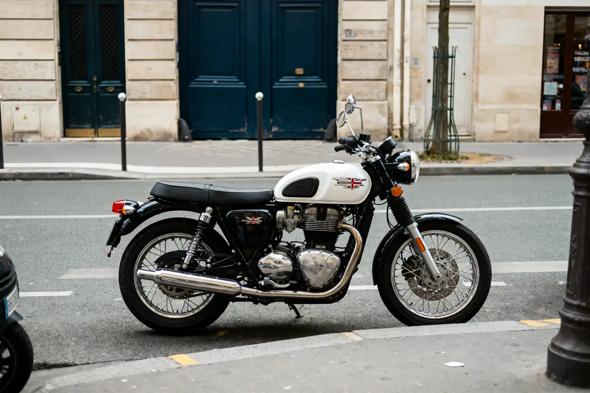 Moto classique blanche stationnée en ville, devant bâtiments historiques en pierre et porte bleue.