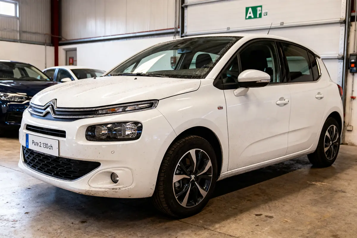 Voiture blanche Citroën garée dans un garage, vue diagonale avant gauche. Autres véhicules stationnés derrière.