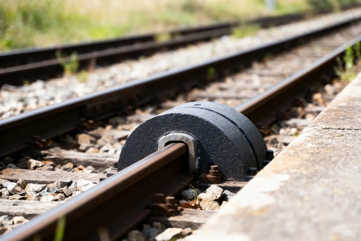 Vue rapprochée d'un butoir de chemin de fer sur des rails avec gravier et herbes environnantes.