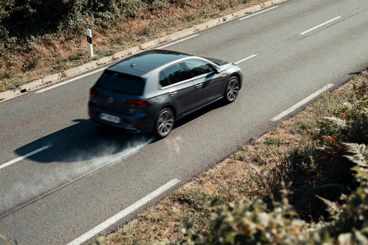 Voiture noire roulant à grande vitesse sur route, laissant traînée de fumée.