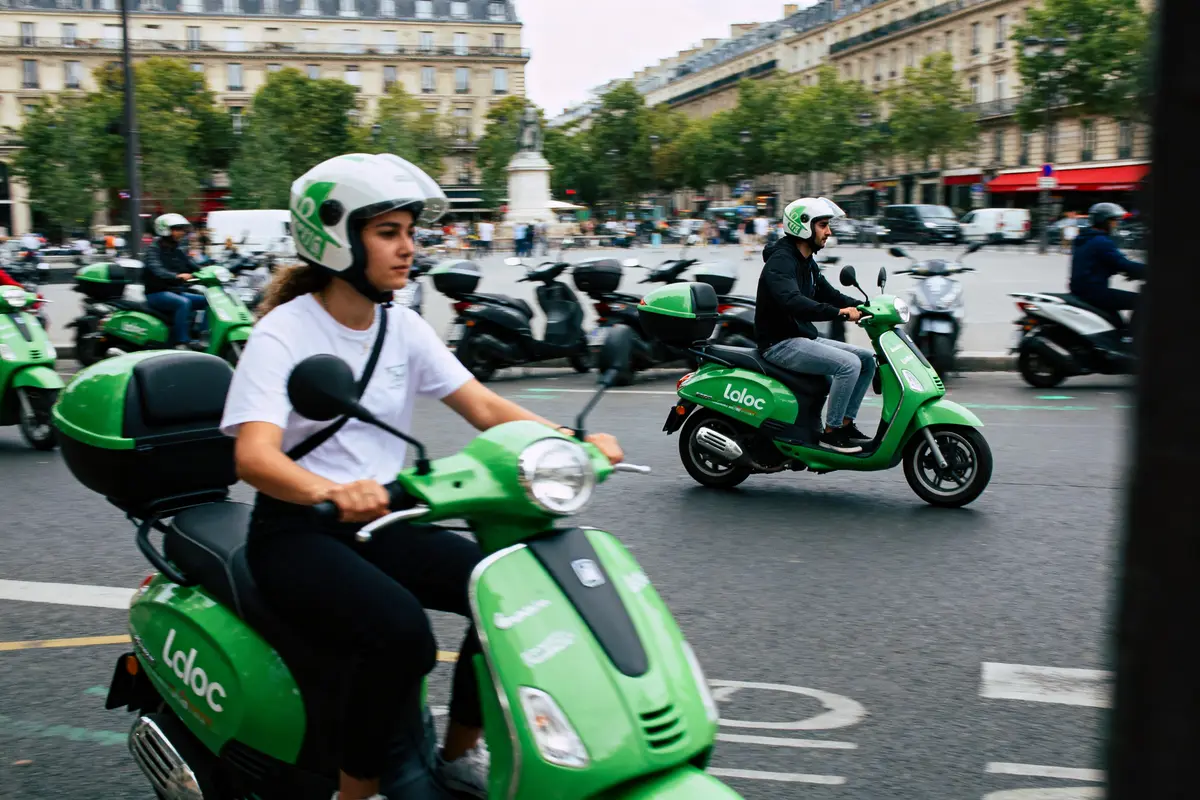 Personnes circulant en scooters verts "Laloc" dans une rue animée d'une ville européenne.