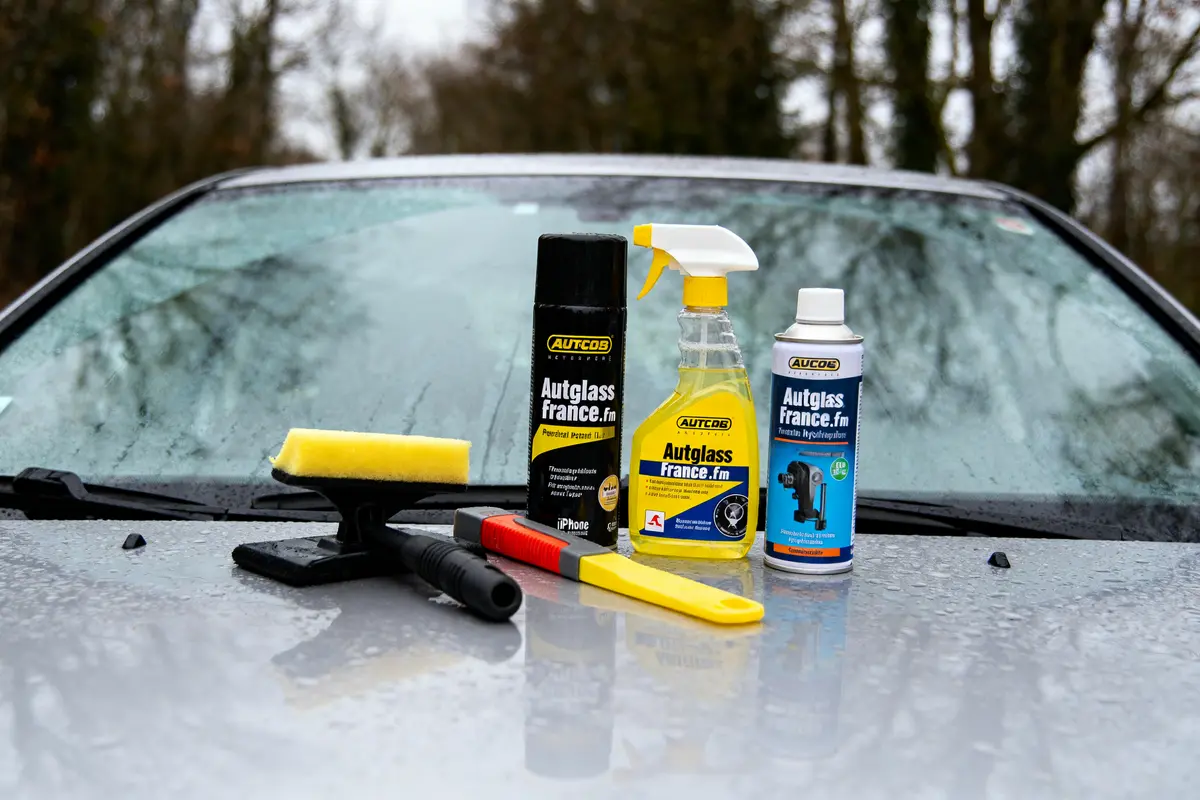 Produits de nettoyage pour pare-brise sur capot de voiture mouillé. Quatre articles visibles, y compris une raclette.