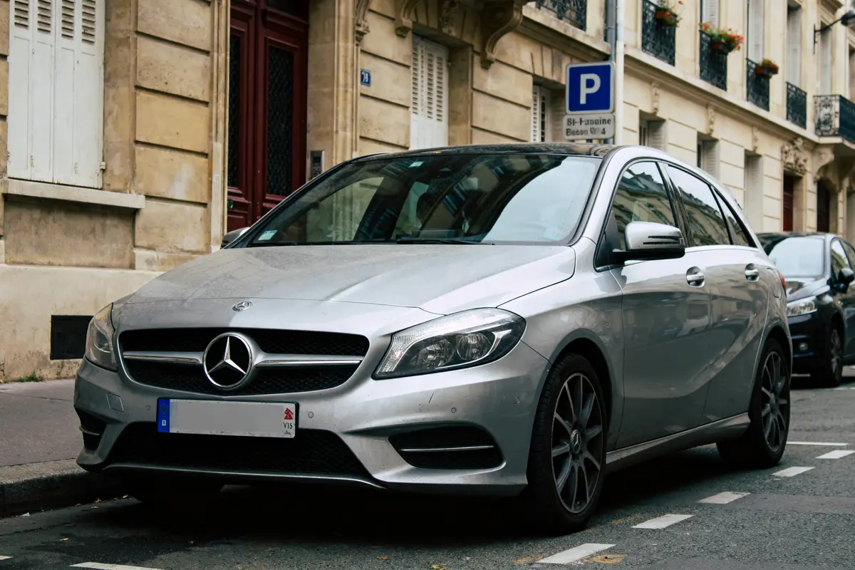 Voiture Mercedes-Benz argentée garée dans une rue, devant des bâtiments anciens avec balcons fleuris.
