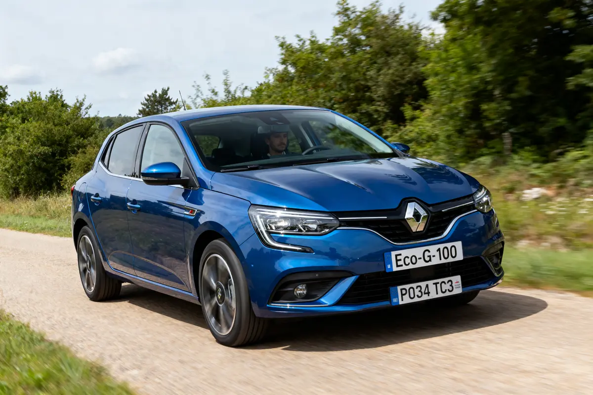 Voiture Renault bleue roulant sur route de campagne bordée de végétation verte.