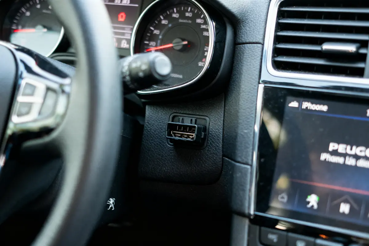 Tableau de bord de voiture avec volant, compteur, prise OBD et écran affichant "iPhone".