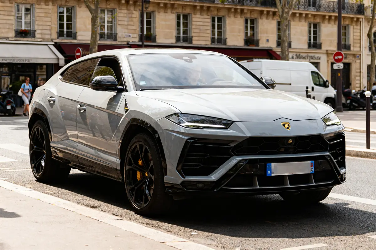 SUV gris de luxe garé en ville, bâtiments anciens en arrière-plan, journée ensoleillée.