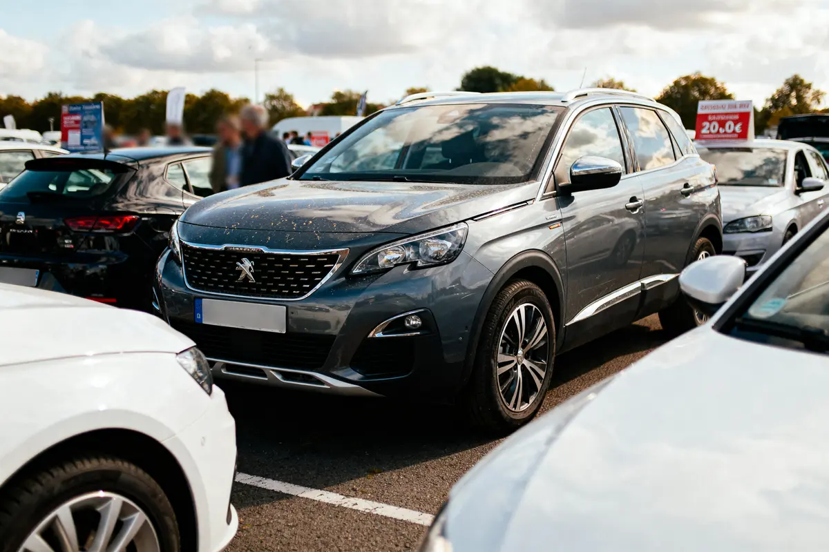 SUV gris Peugeot garé sur un parking, entouré d'autres voitures, sous ciel nuageux.