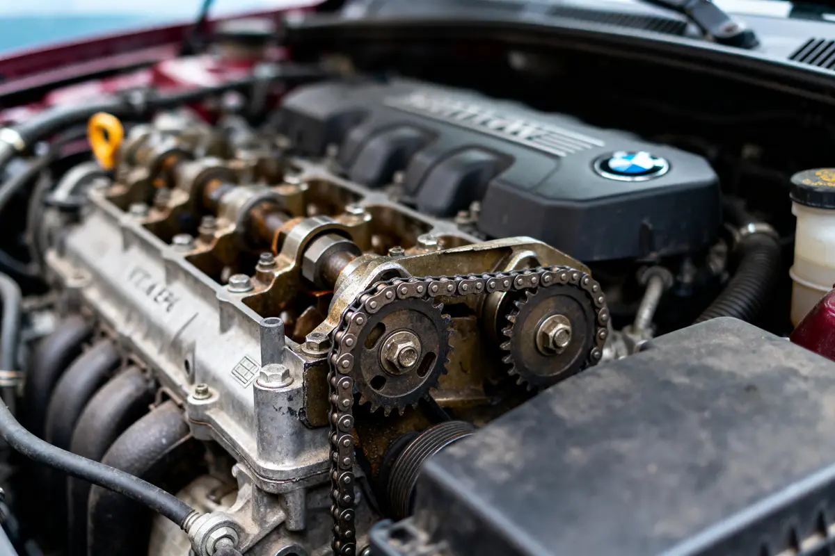 Moteur de voiture BMW, chaînes et cames visibles dans le compartiment moteur ouvert.