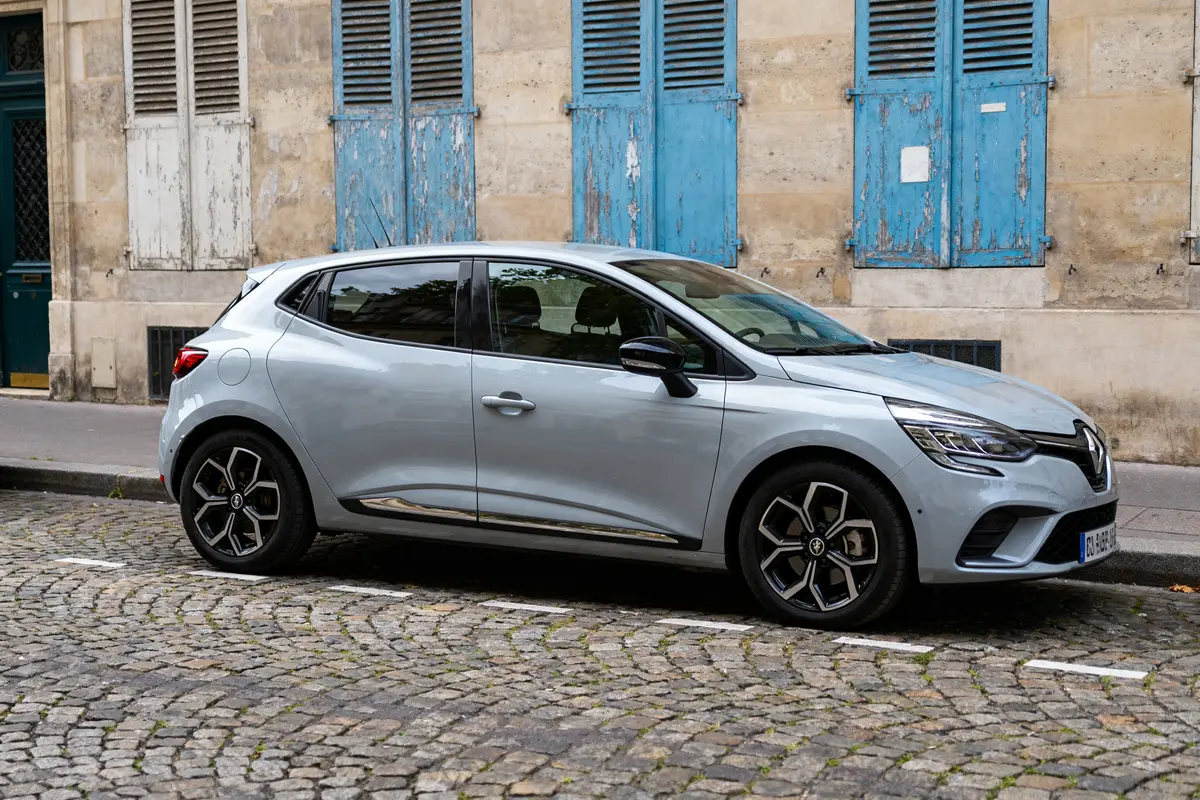 Voiture Renault Clio 6 grise stationnée devant mur beige et volets bleus