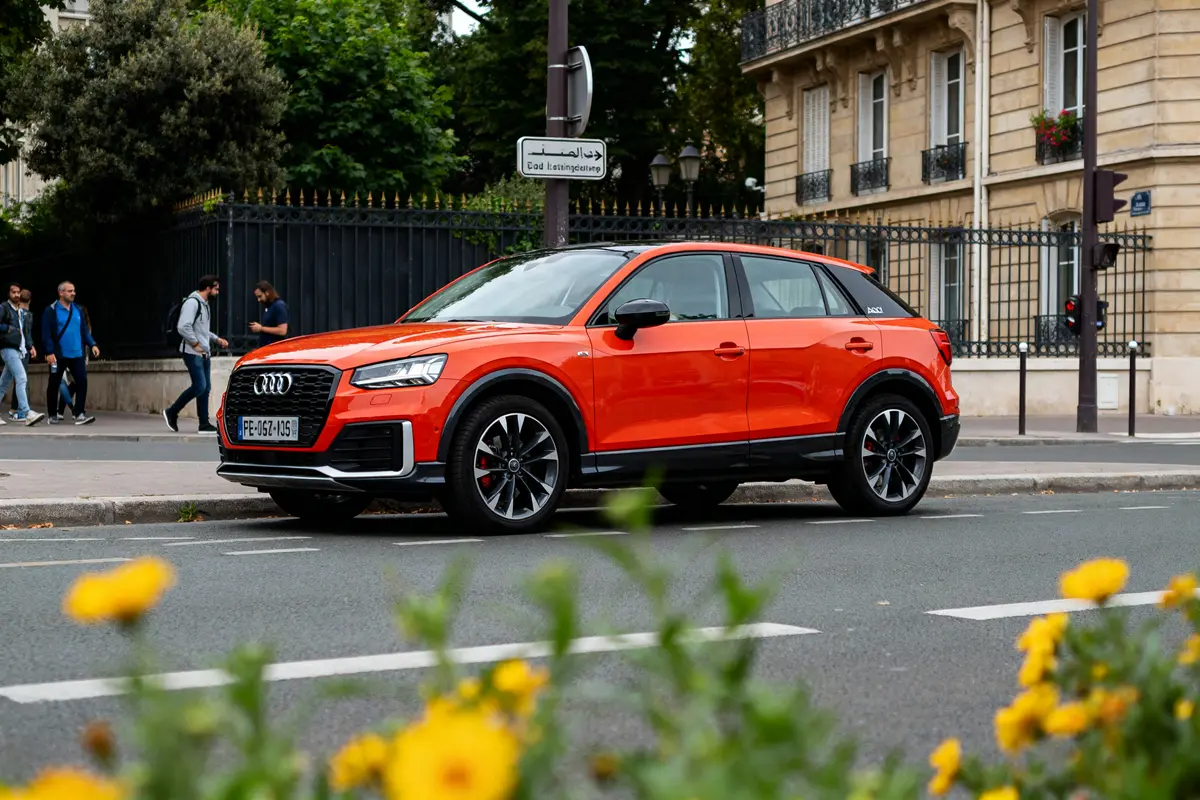 Audi Q2 orange en ville derrière des fleurs jaunes audi q2 avis