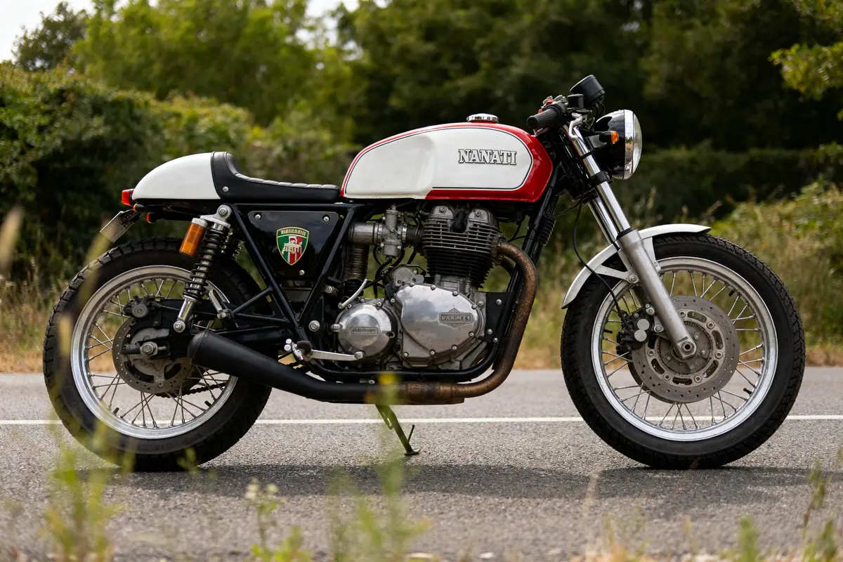 Moto classique sur route arborée, représentant une marque de moto italienne vintage prestigieuse.