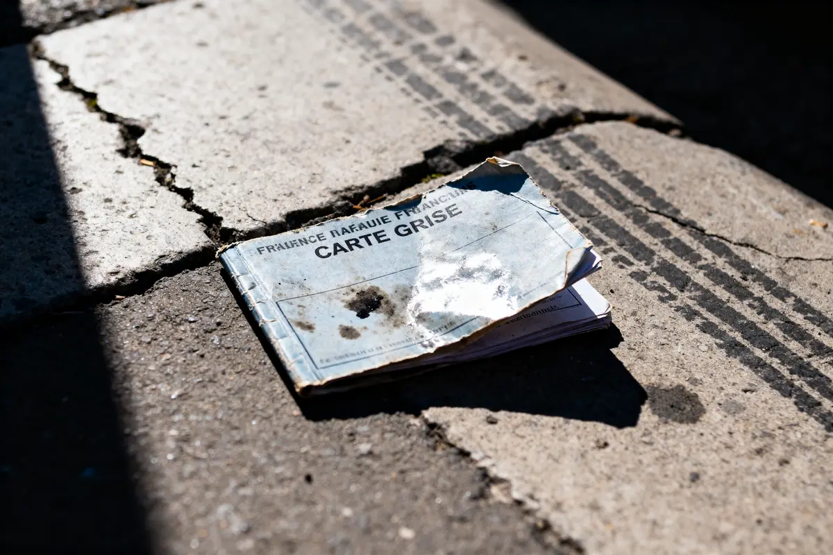 Carte grise abîmée sur trottoir avec traces et fissures, éclairée par le soleil.