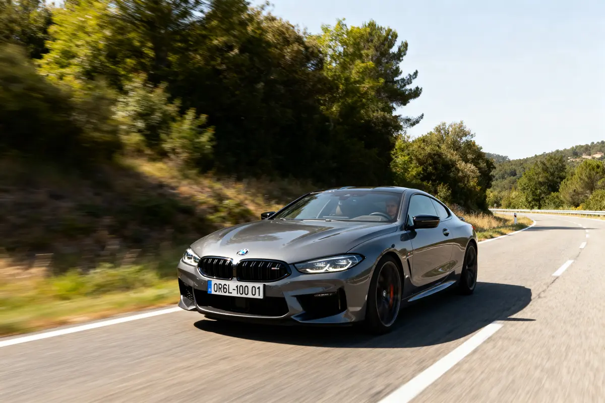 Voiture grise BMW roulant sur une route bordée d’arbres, par une journée ensoleillée.