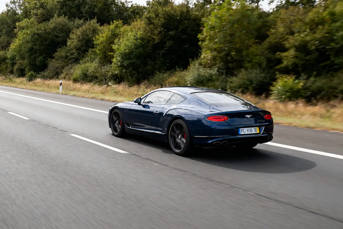 Voiture bleue de luxe sur l'autoroute, entourée de végétation, roulant vers l'horizon.