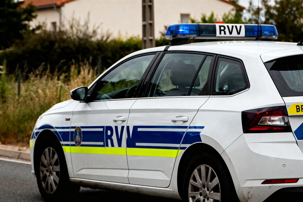 Voiture de police avec gyrophare bleu et marquages "RVV", stationnée près d'une route.