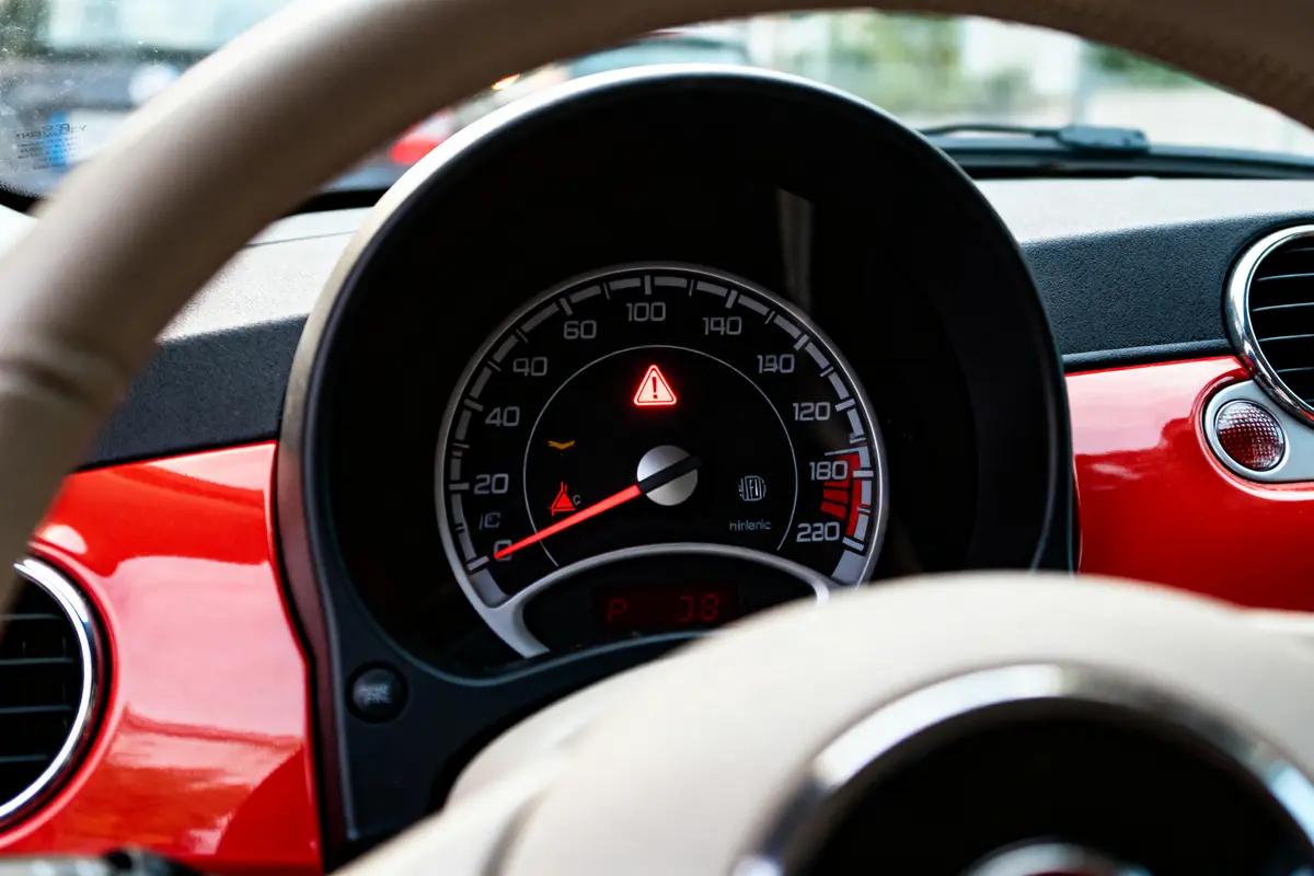 Tableau de bord d'une voiture avec voyant d'avertissement allumé, compteur de vitesse jusqu'à 220 km/h.