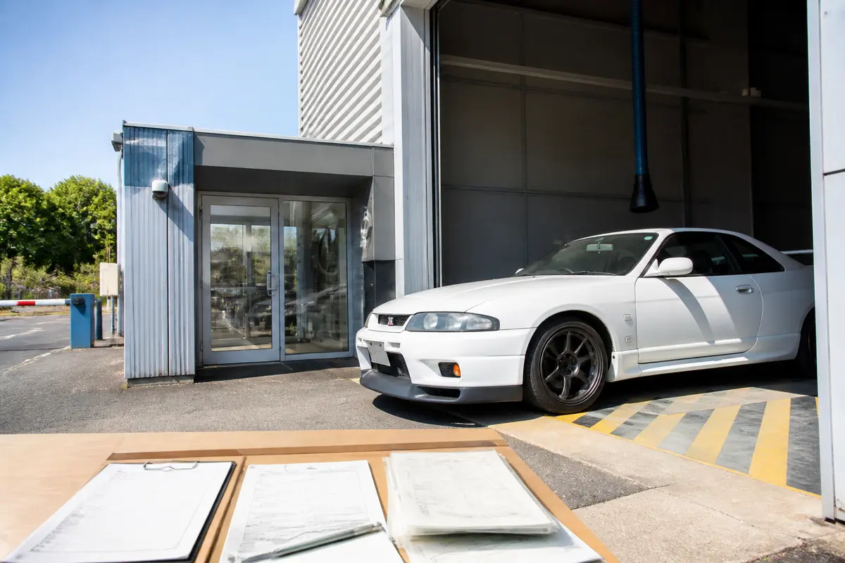 Voiture blanche sortant d'un garage avec documents pour importer une voiture du Japon visibles